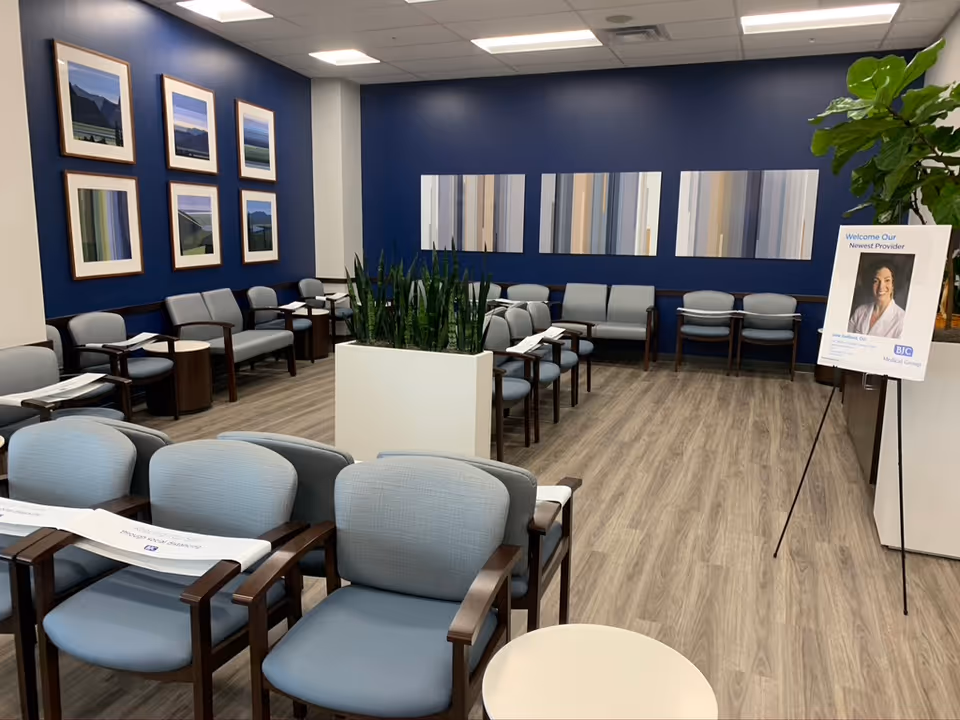 A clinic waiting area with blue walls, plants, and numerous gray chairs.