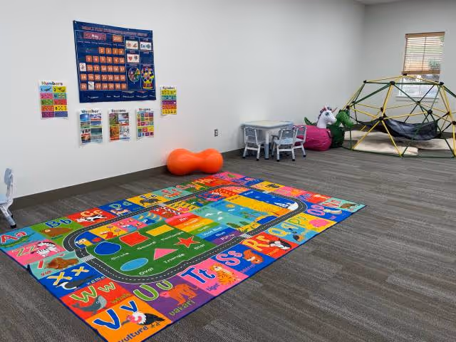 Colorful children's play area with alphabet rug, small table, climbing dome, and toys.