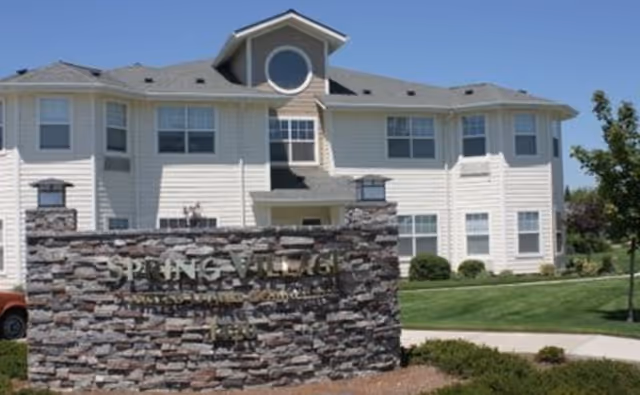 Two-story light-gray senior living building with a stone entrance sign.
