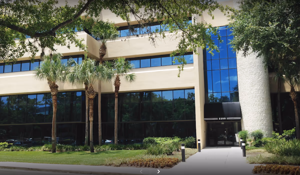 Exterior of a modern building with glass windows, palm trees, and a front entrance.
