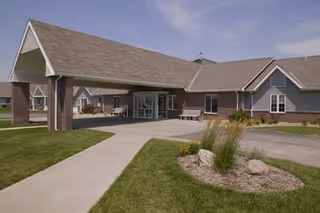 Single-story senior living facility entrance with a covered drive, brick exterior, and landscaped front.