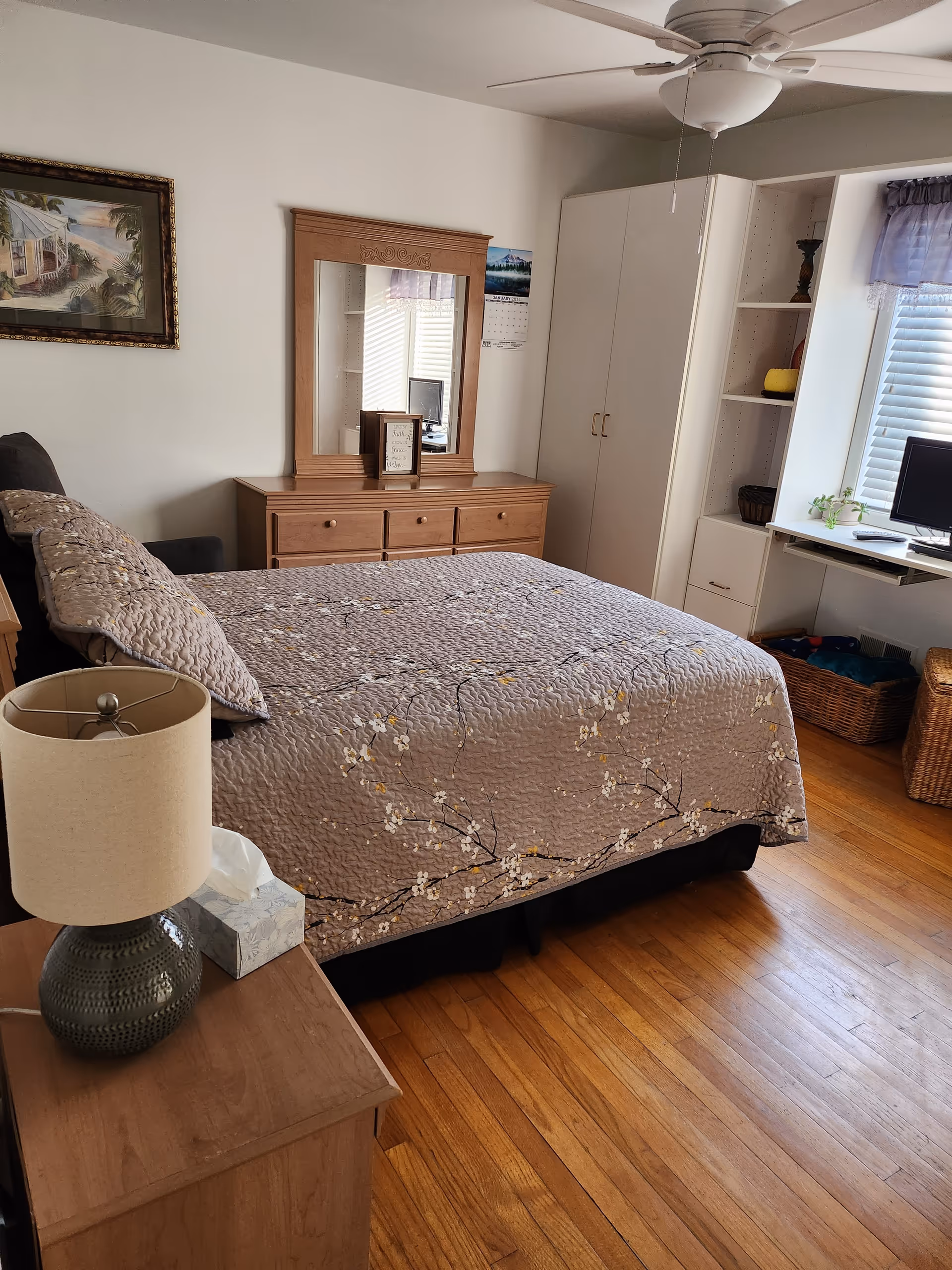 A tidy bedroom with a bed, dresser, mirror, desk, and ceiling fan.