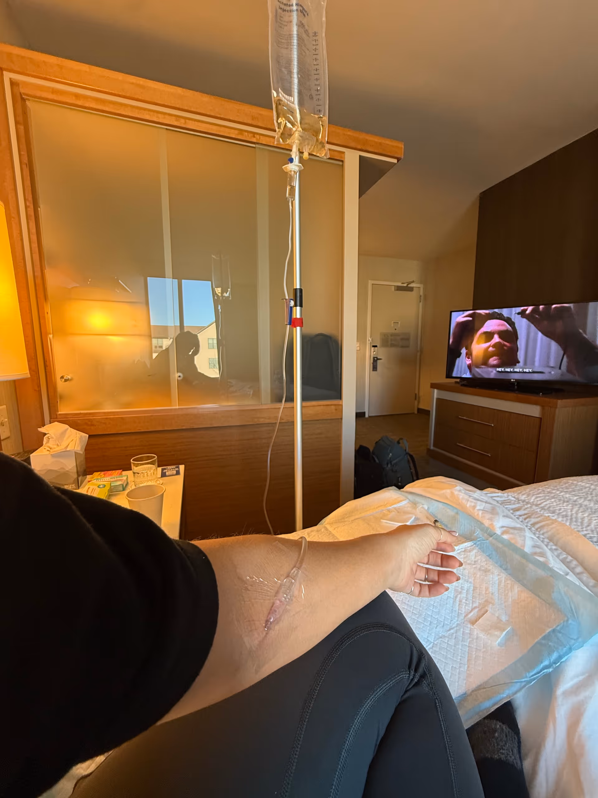 Arm with IV infusion resting on bed in a hospital-style room.