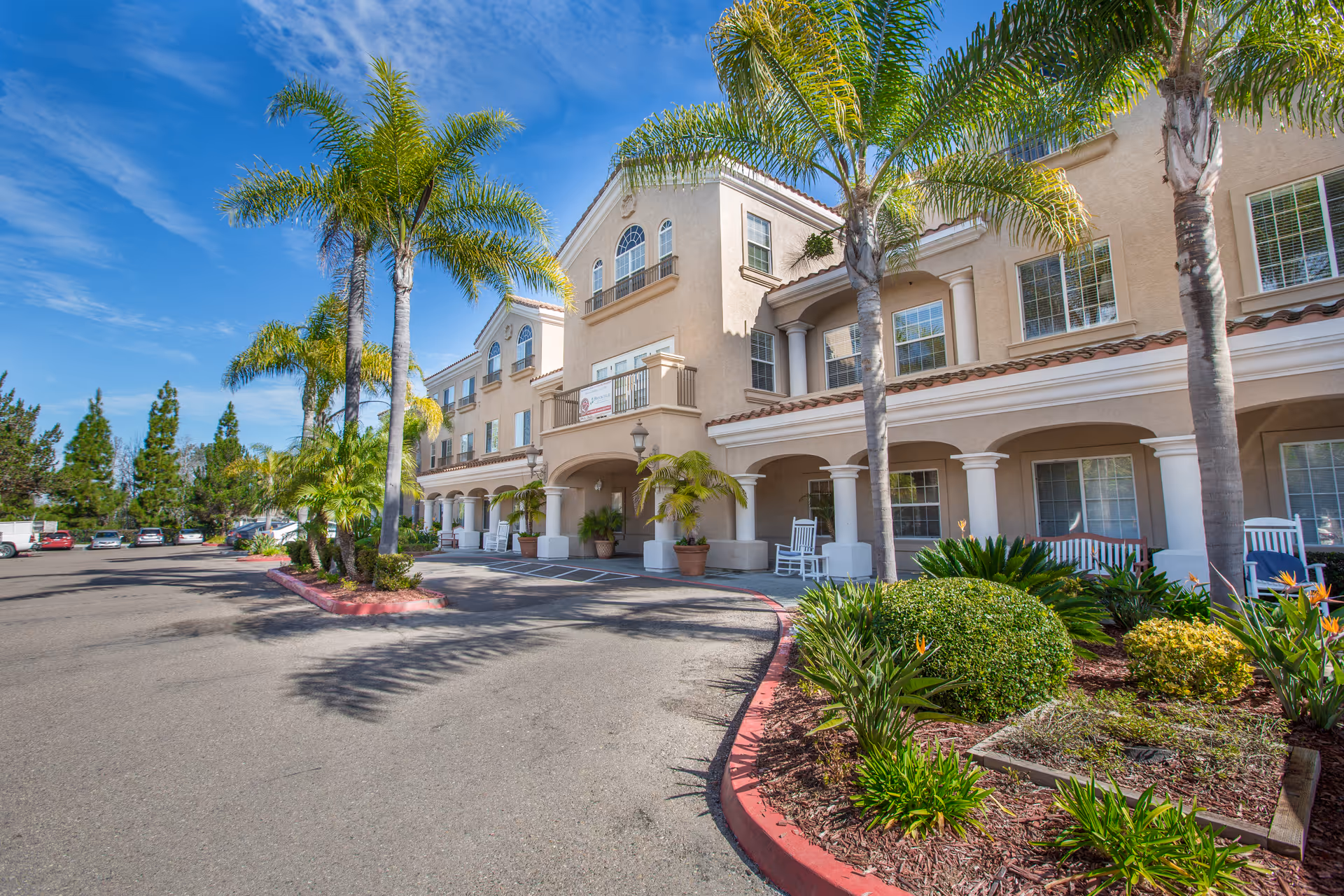 Exterior view of Bayshire Torrey Pines with palm trees and a curved entrance.