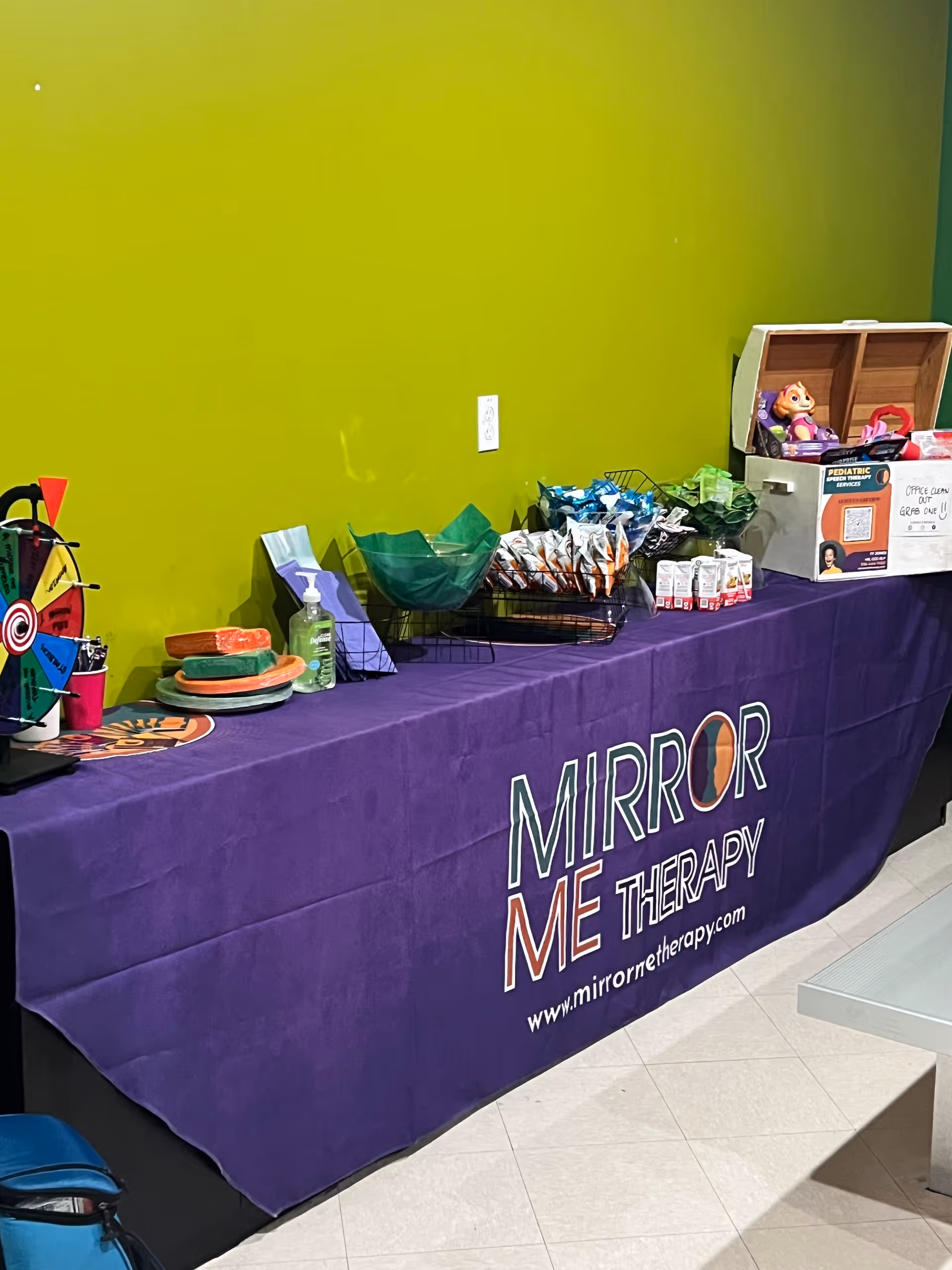Promotional Mirror Me Therapy table with items and toys against a bright green wall.
