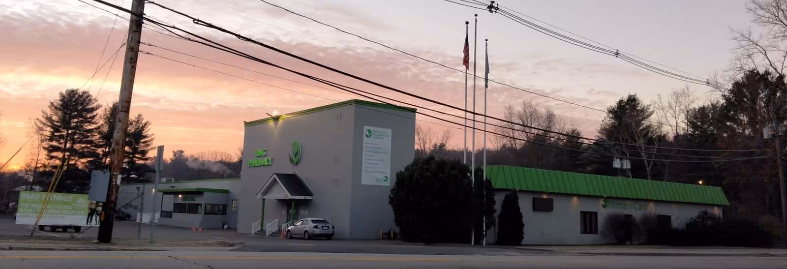Exterior view of a white and green medical facility on a street at sunset.