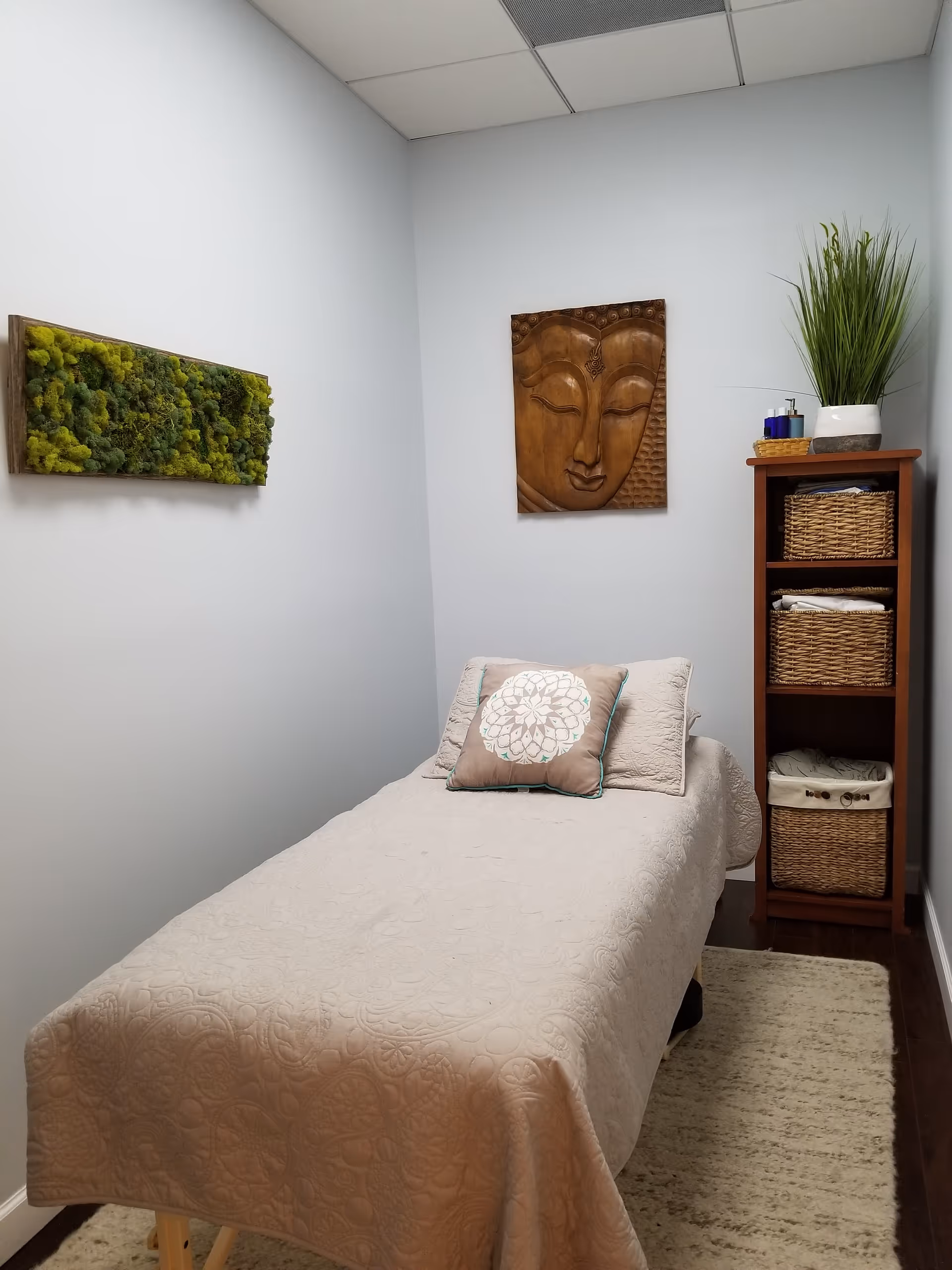 A small therapy room with a padded treatment bed, pillows, and Buddha wall art.