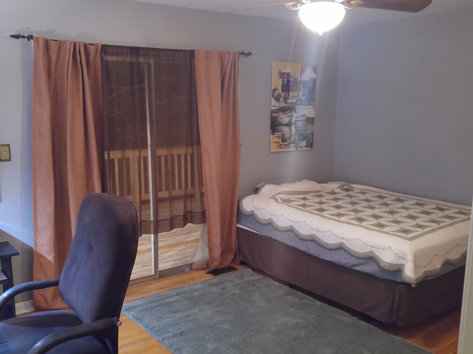 Blue-walled bedroom with a bed, sliding glass door, pink curtains, and a blue rug.