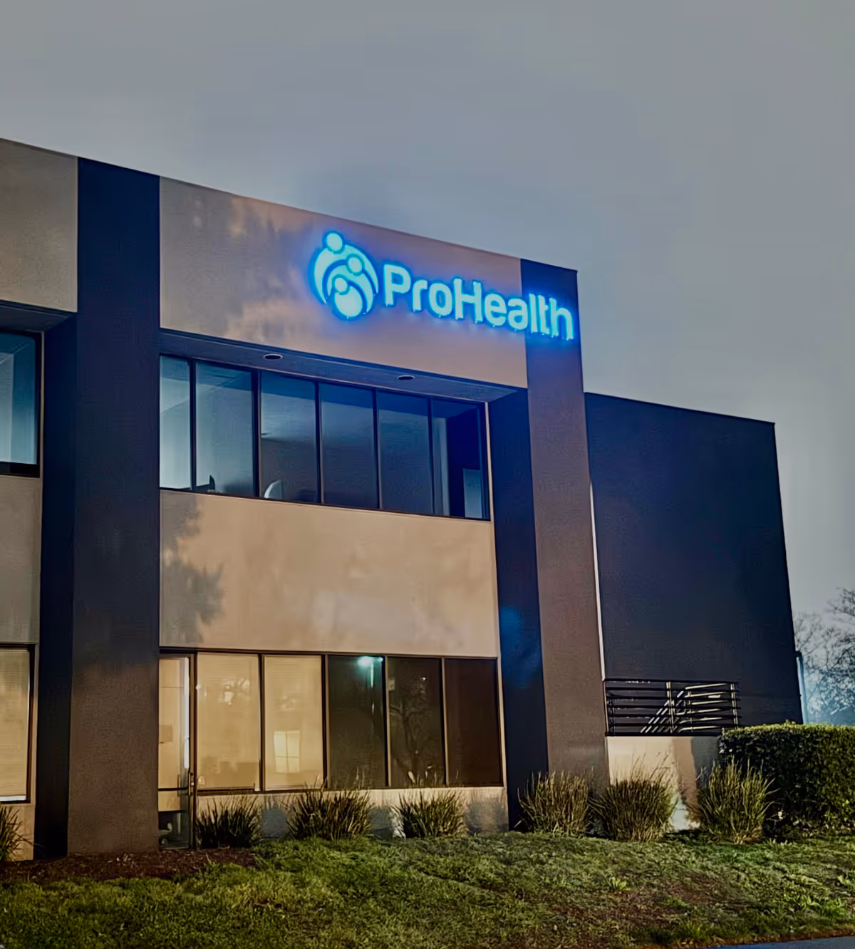 Exterior front of a ProHealth building with a blue illuminated logo.