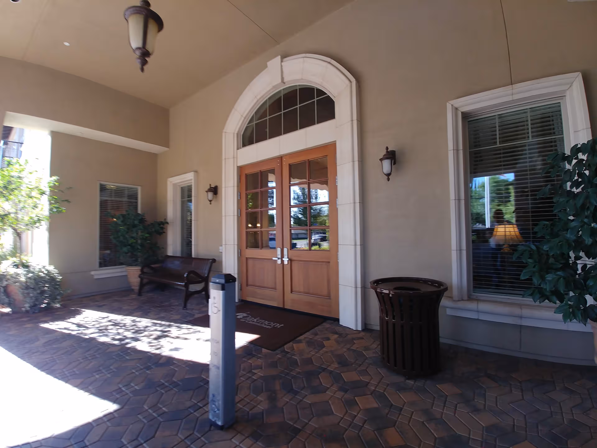 Oakmont of Carmichael entryway with double wooden doors, bench, potted plants, and tiled porch.