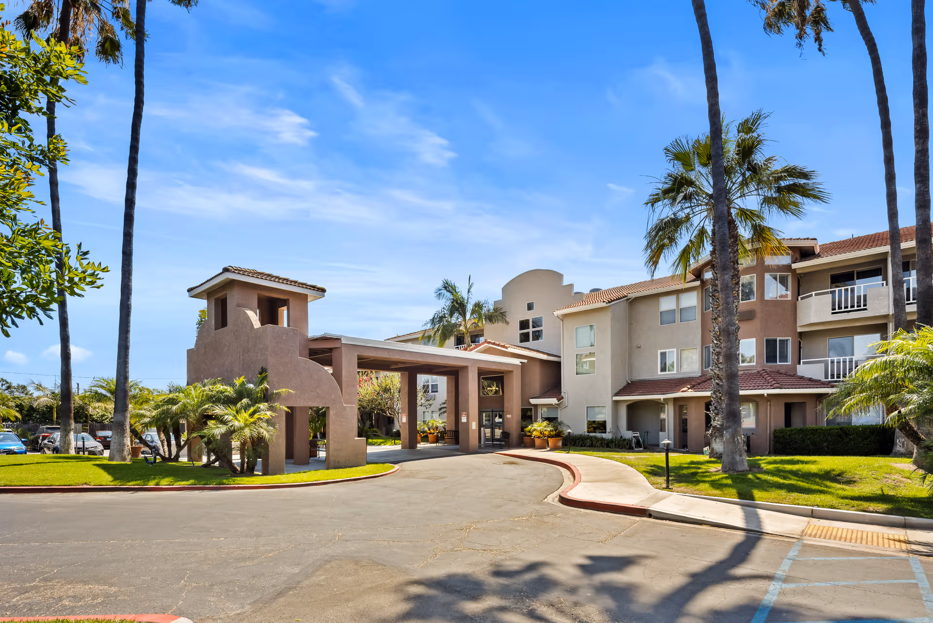 Exterior view of La Mirada Heights senior living facility with palm trees and a covered entrance.