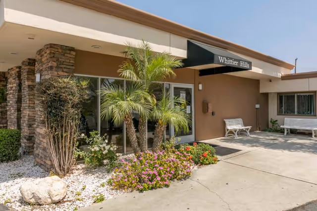 Exterior entrance of Whittier Hills with an awning reading "Whittier Hills," landscaping, and benches.