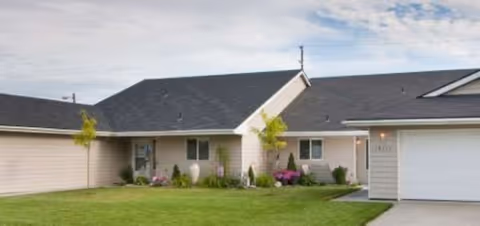 Front view of a single-story senior living home with lawn, shrubs, and a driveway.