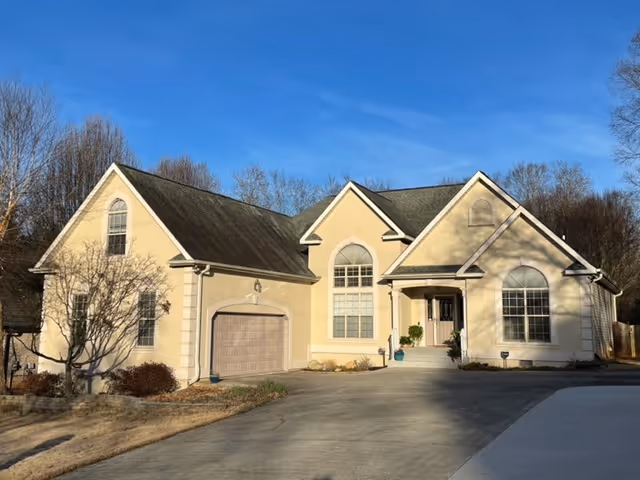 Residential-style senior living facility exterior with beige stucco, two gabled roofs, and a driveway.