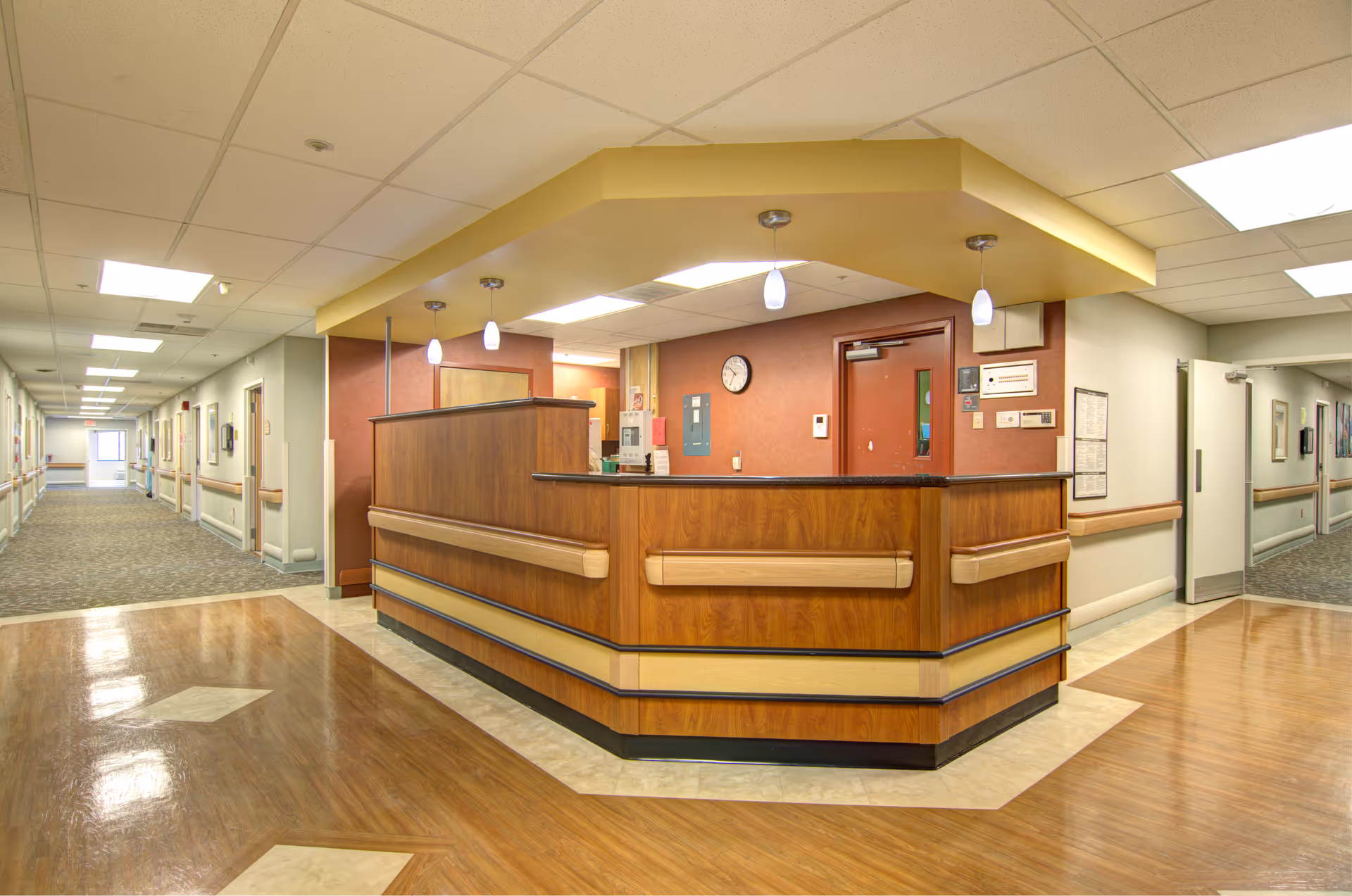 Wood-paneled reception desk in a well-lit senior care facility lobby with hallways.