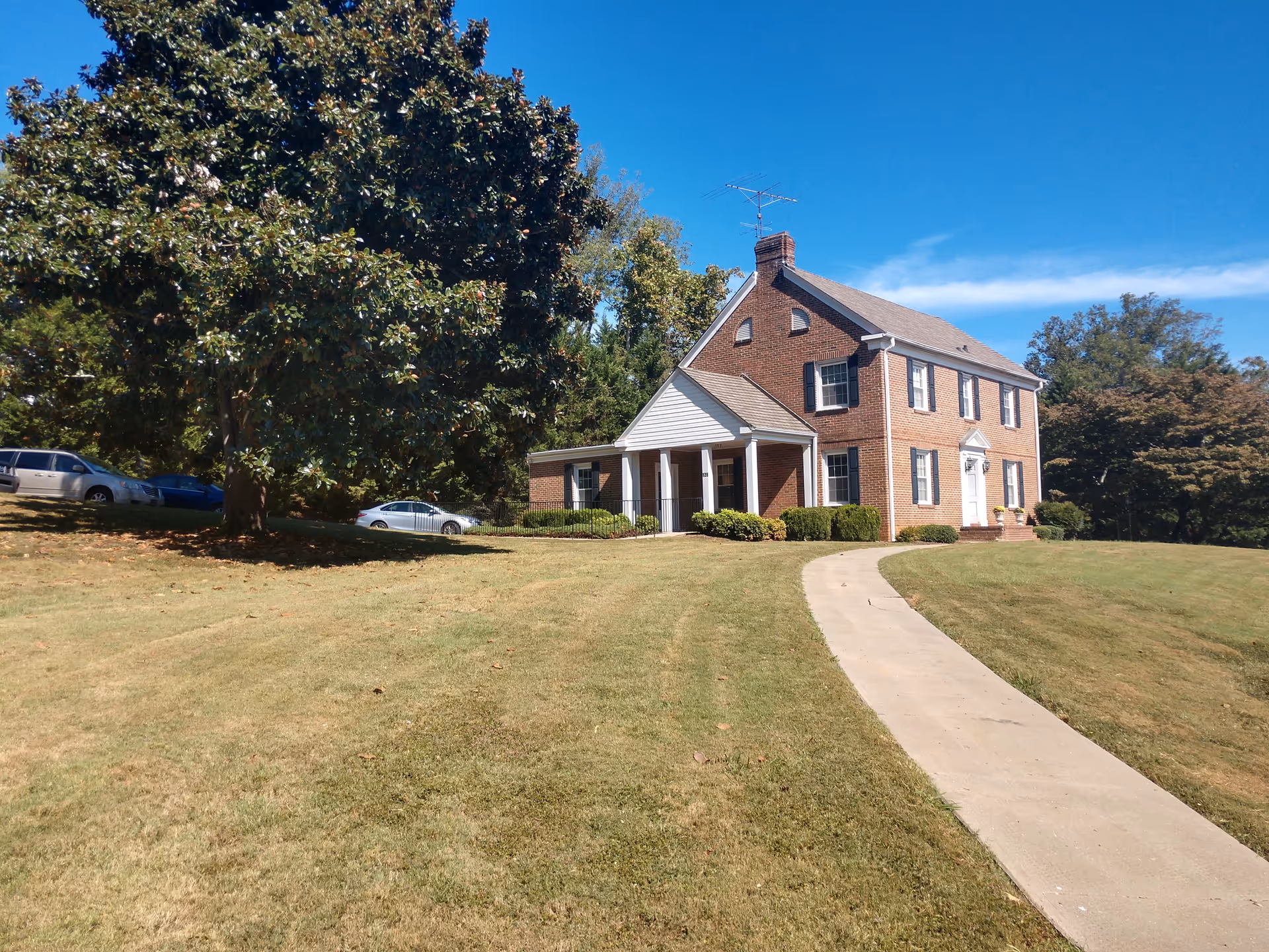 Brick senior living facility exterior with front lawn, curved walkway, and cars.
