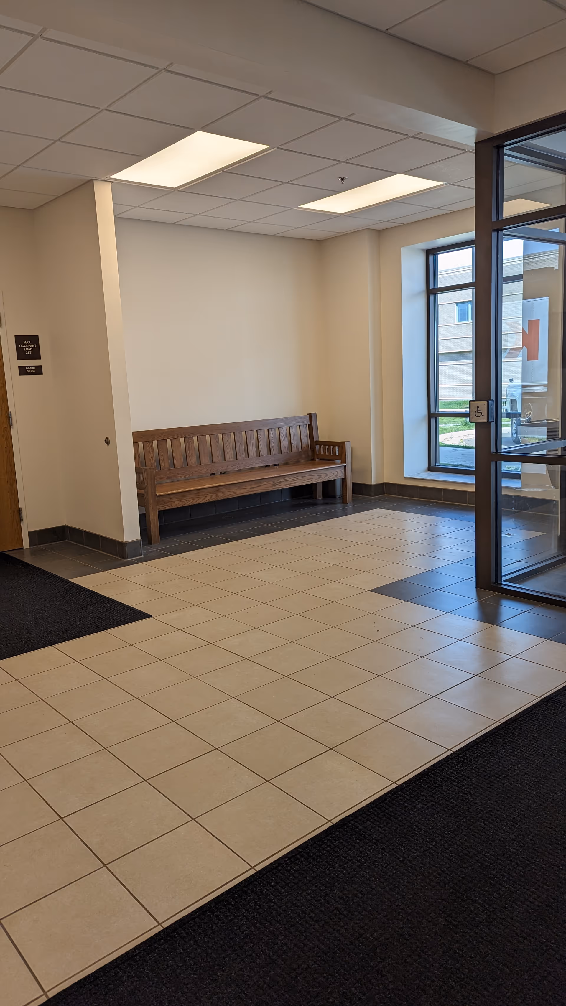 Lobby area with a wooden bench, tiled floor, and glass entrance doors.