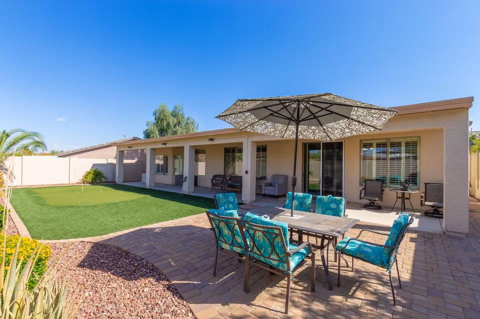 Sunny outdoor patio at a single-story assisted living facility with seating and umbrella.