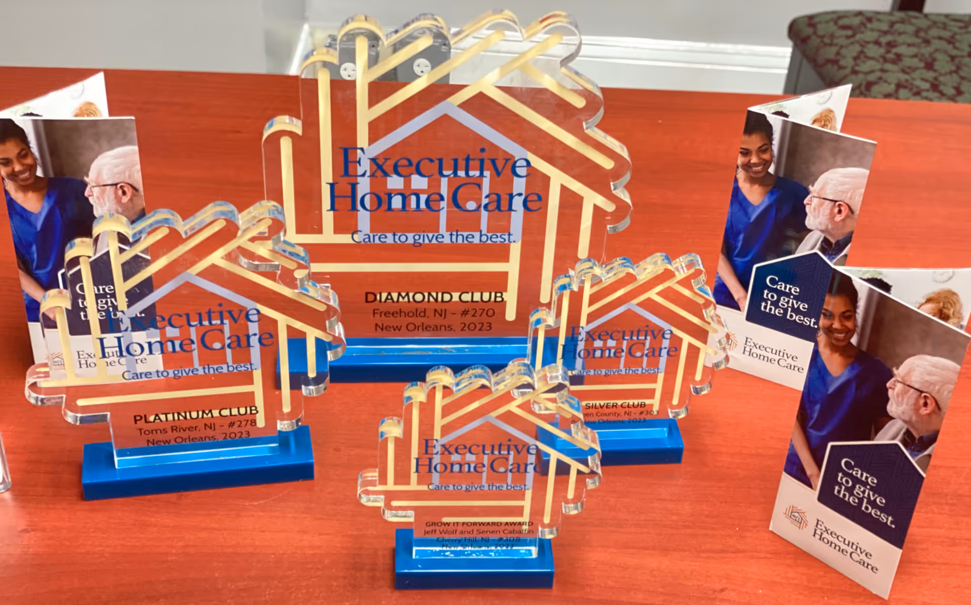Glass trophy awards with Executive Home Care branding arranged on a wooden table.