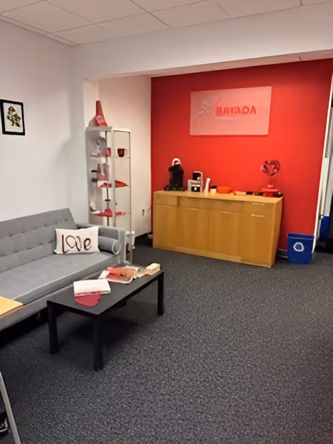 Cozy lobby area with gray sofa, coffee table, and a red accent wall behind reception desk.
