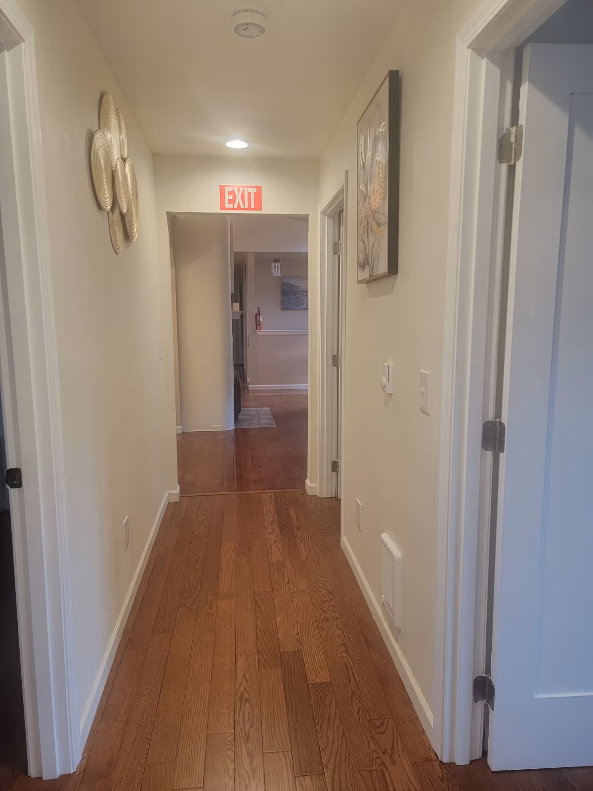Well-lit interior hallway at Amana Adult Family Home with wooden floors and exit sign.