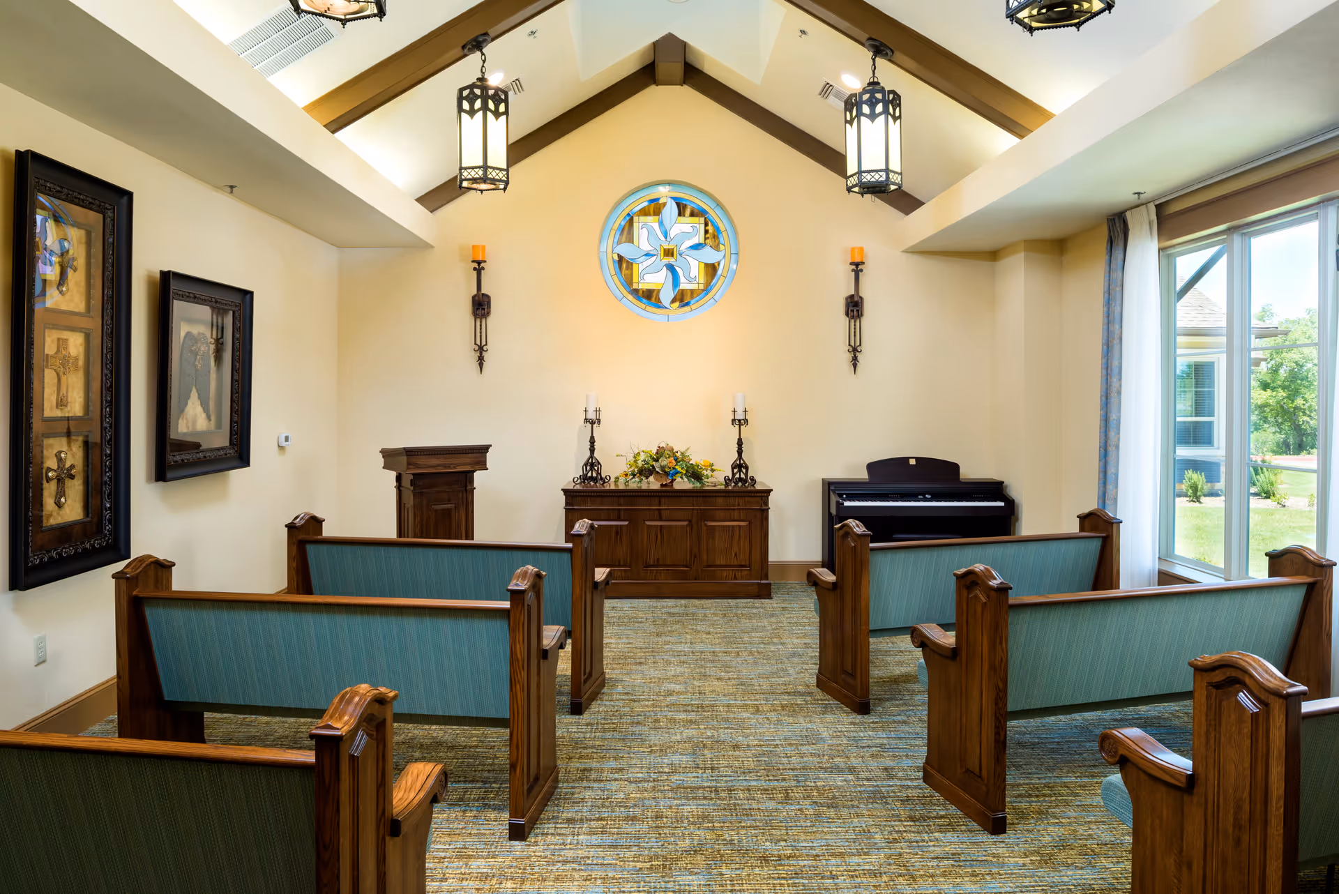 Small chapel-style interior with wooden pews facing an altar, a round stained-glass window, and a piano by the window.