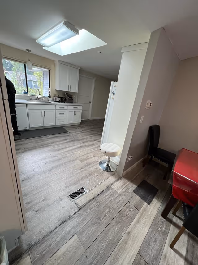 Bright compact kitchen with white cabinets, sink, fridge, window, and a small white stool.