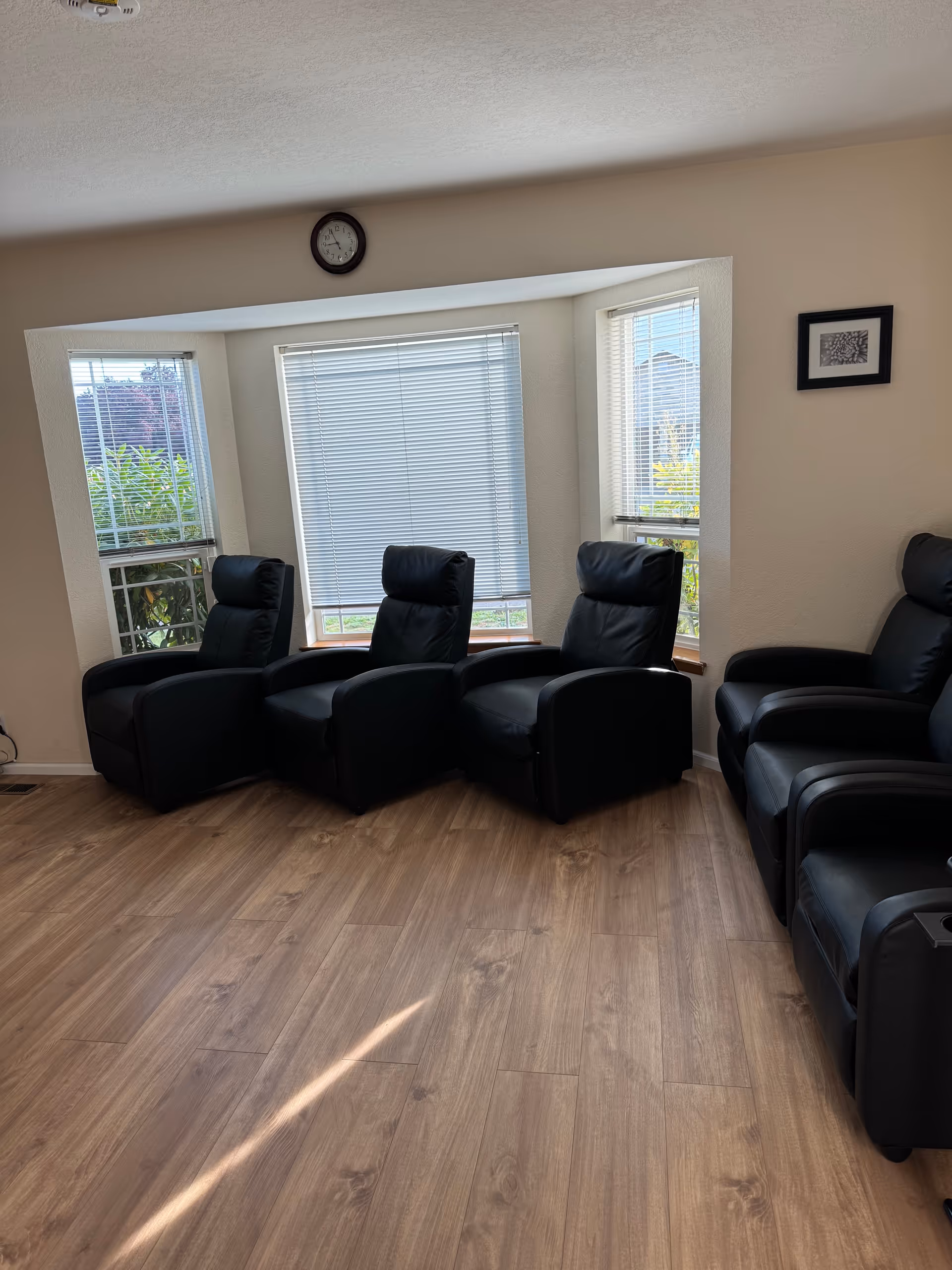 Row of black recliners along windows in a cozy, well-lit common living room.