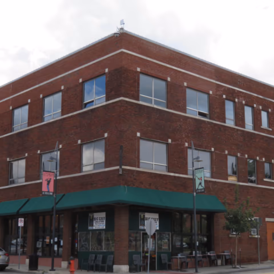 Brick three-story building with green awning storefront and outdoor seating along sidewalk.