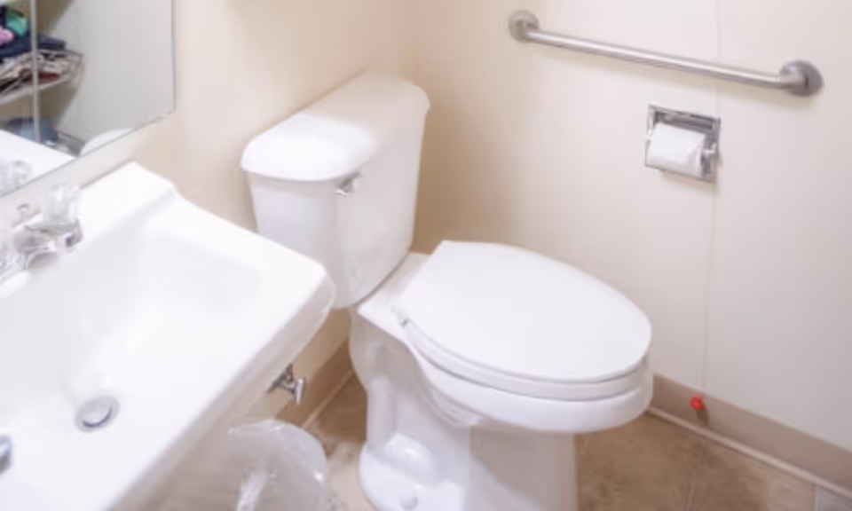 White bathroom with sink, toilet, and wall grab bar in a senior facility.