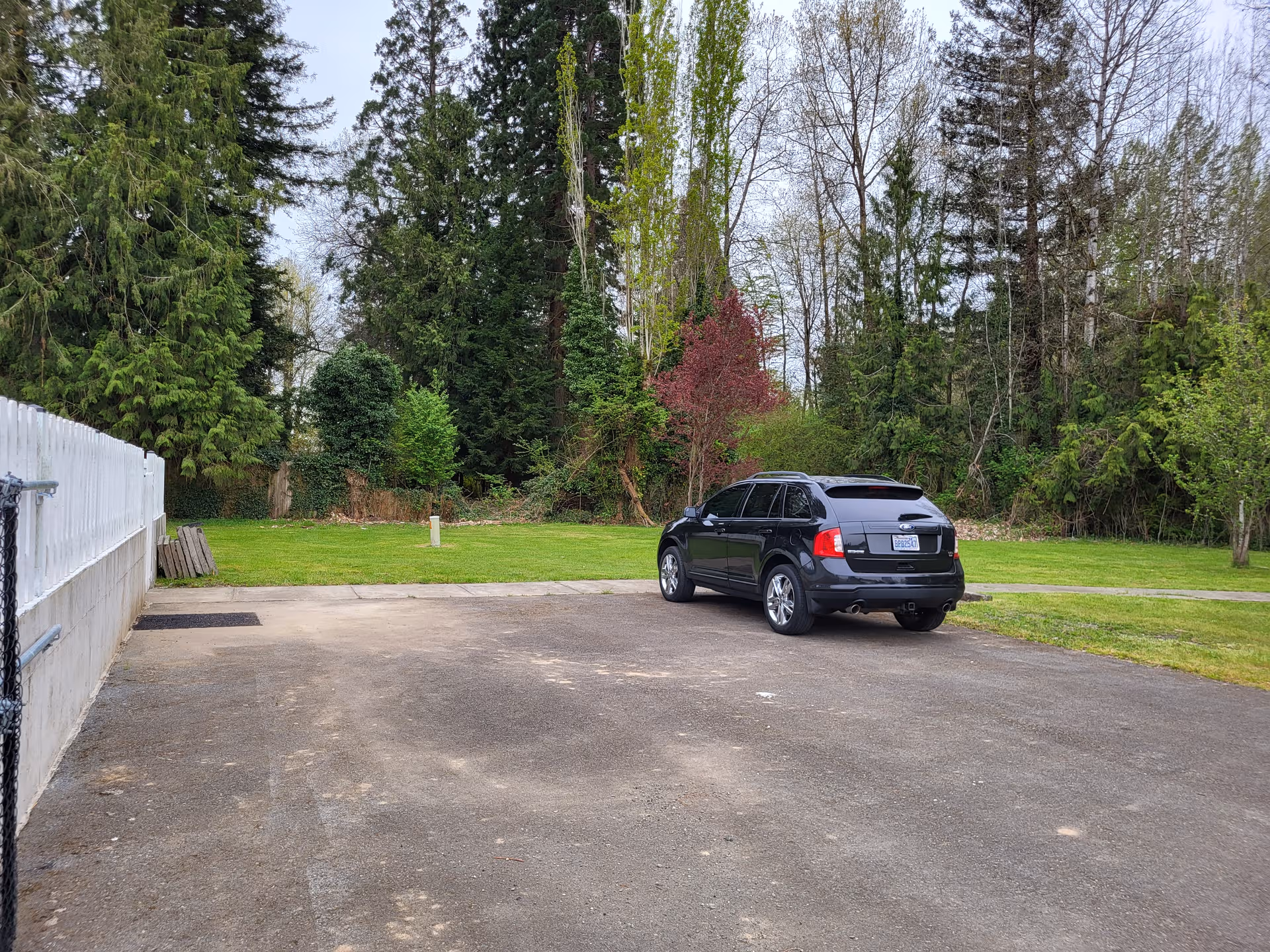 Black SUV parked on a paved lot beside a grassy, tree-lined area.