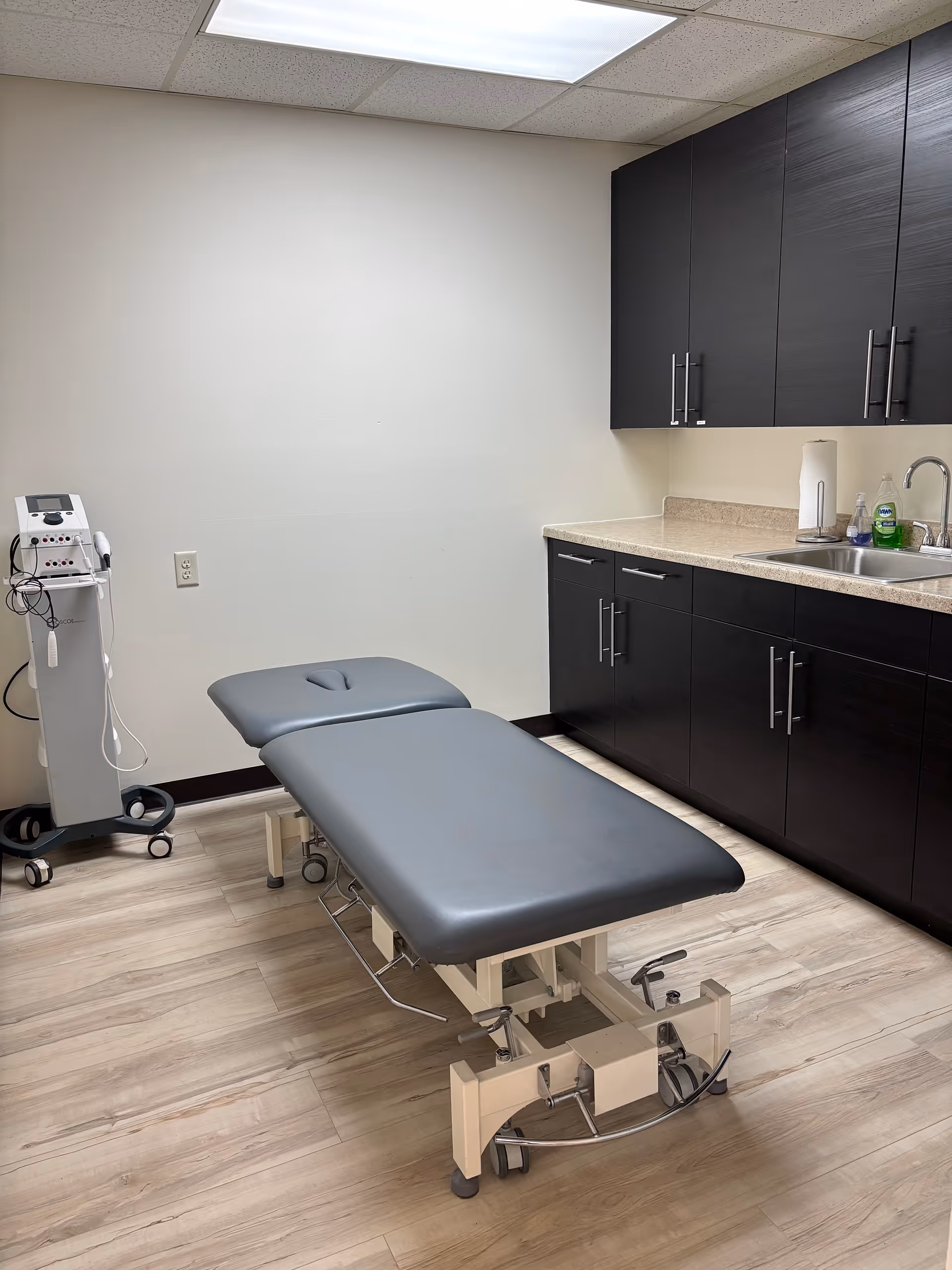 Clinical therapy room with adjustable exam table, sink, and dark cabinets.