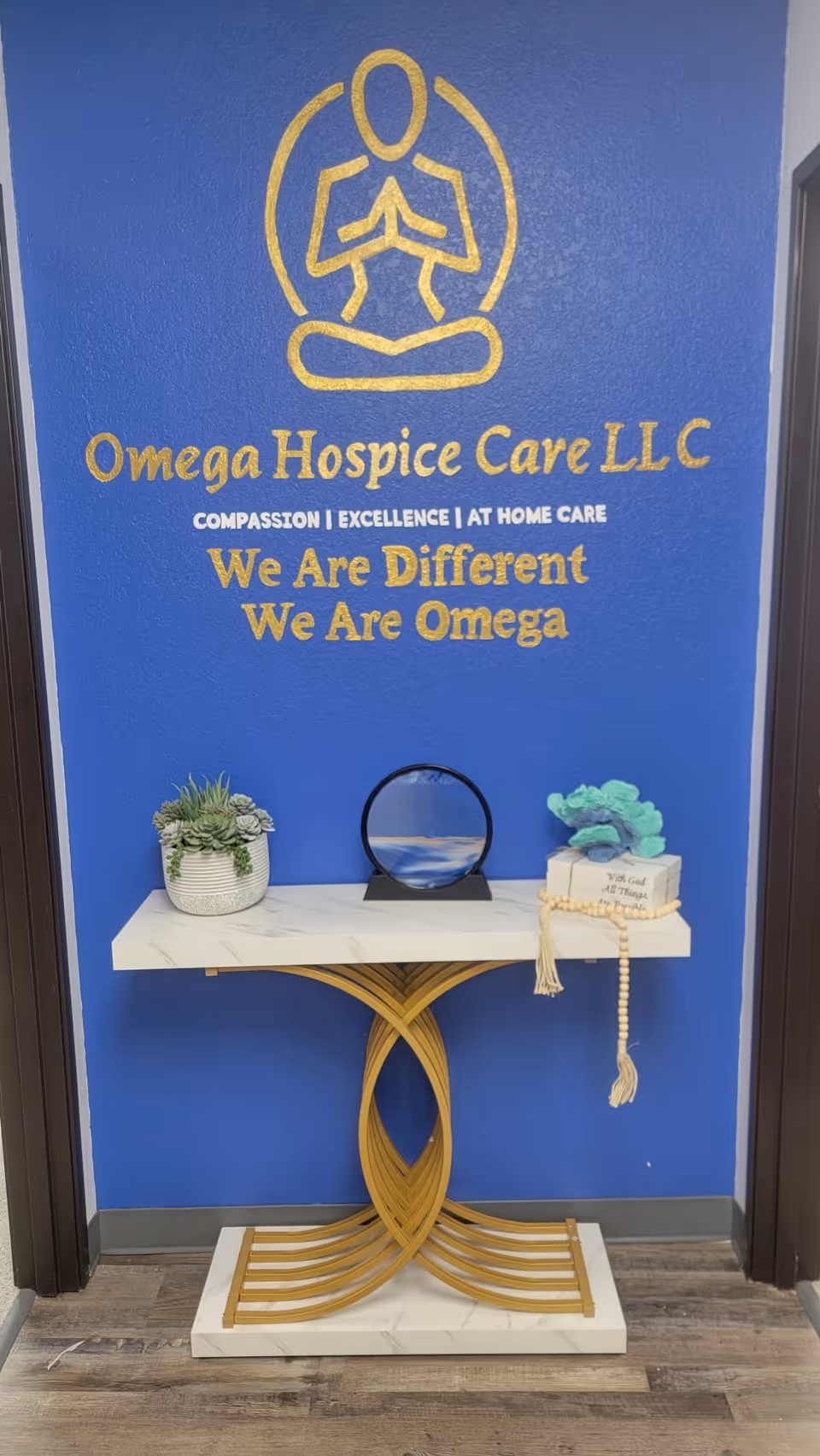 Blue wall with Omega Hospice Care LLC logo and a decorative console table in a lobby.