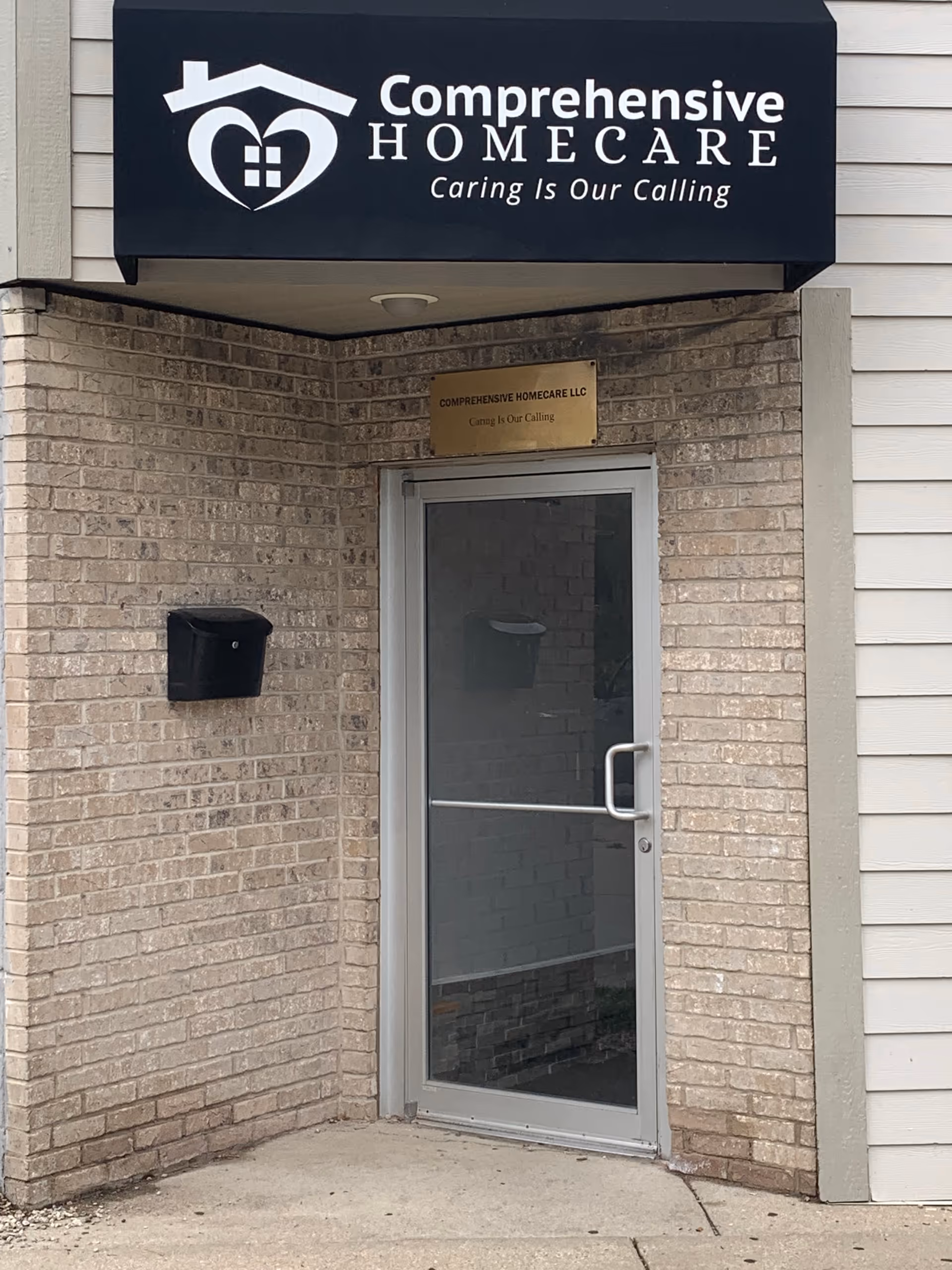 Exterior brick entrance with glass door, canopy sign reading Comprehensive Home Care.
