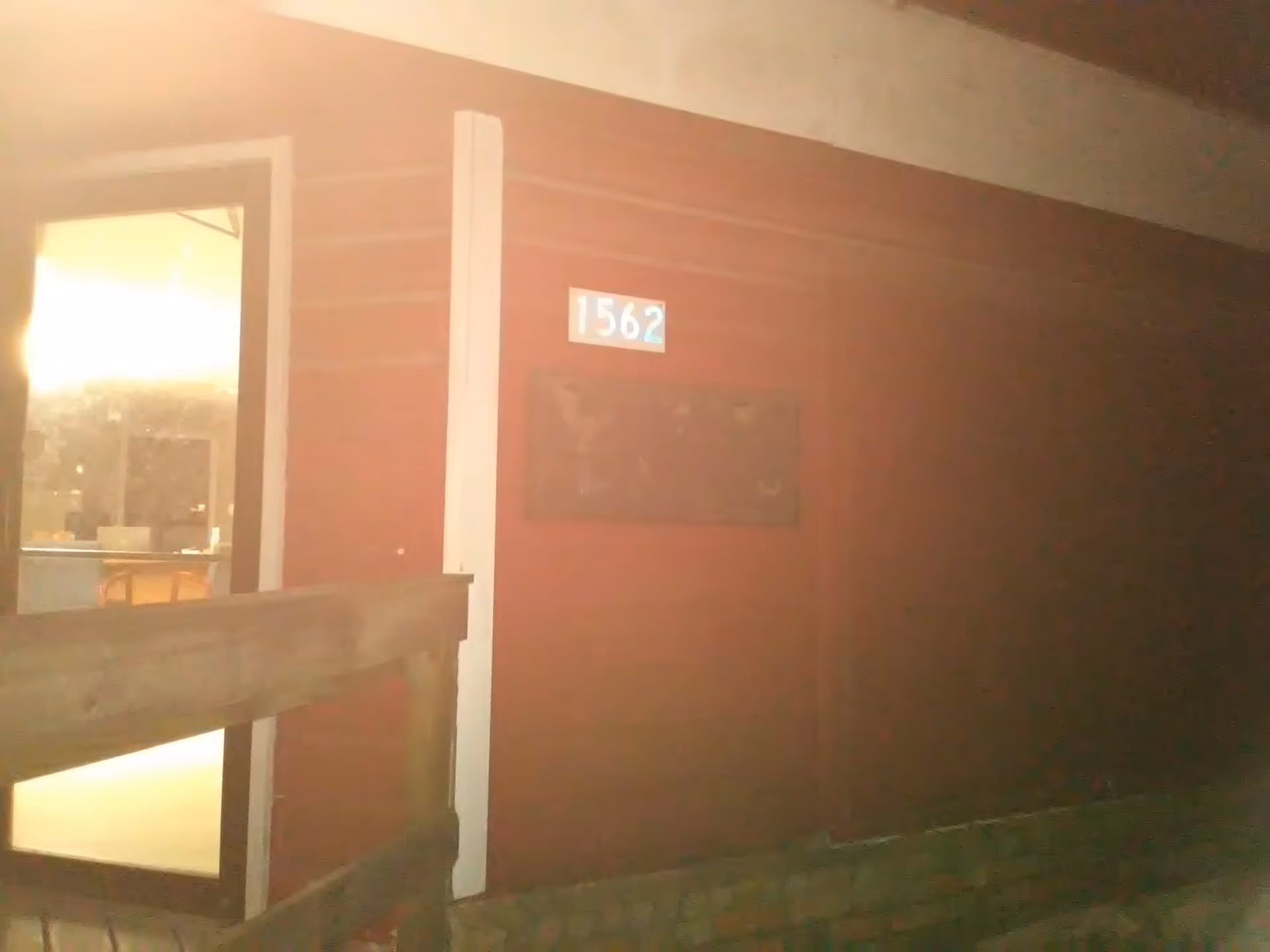 Night exterior of a red building with a door, window, and a blue 1562 plaque.
