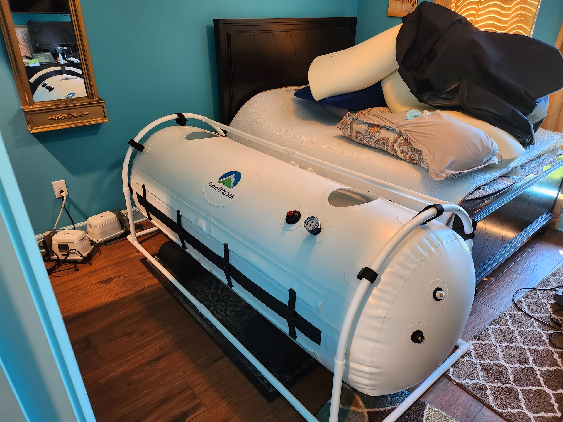 Large white hyperbaric chamber sits beside a bed in a teal-painted bedroom.