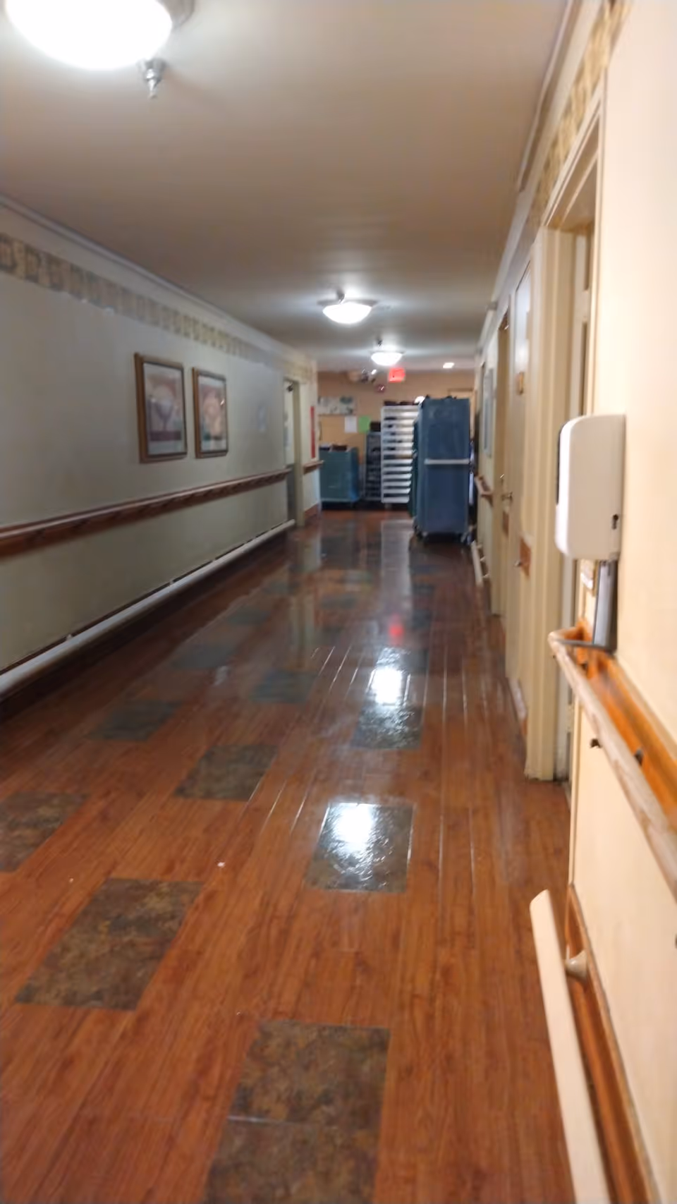 Long interior hallway in a senior living facility with wood-like floor and overhead lights