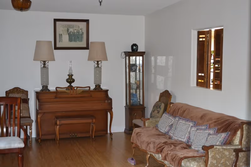 Traditional living room with sofa, piano, lamps, and display cabinet.