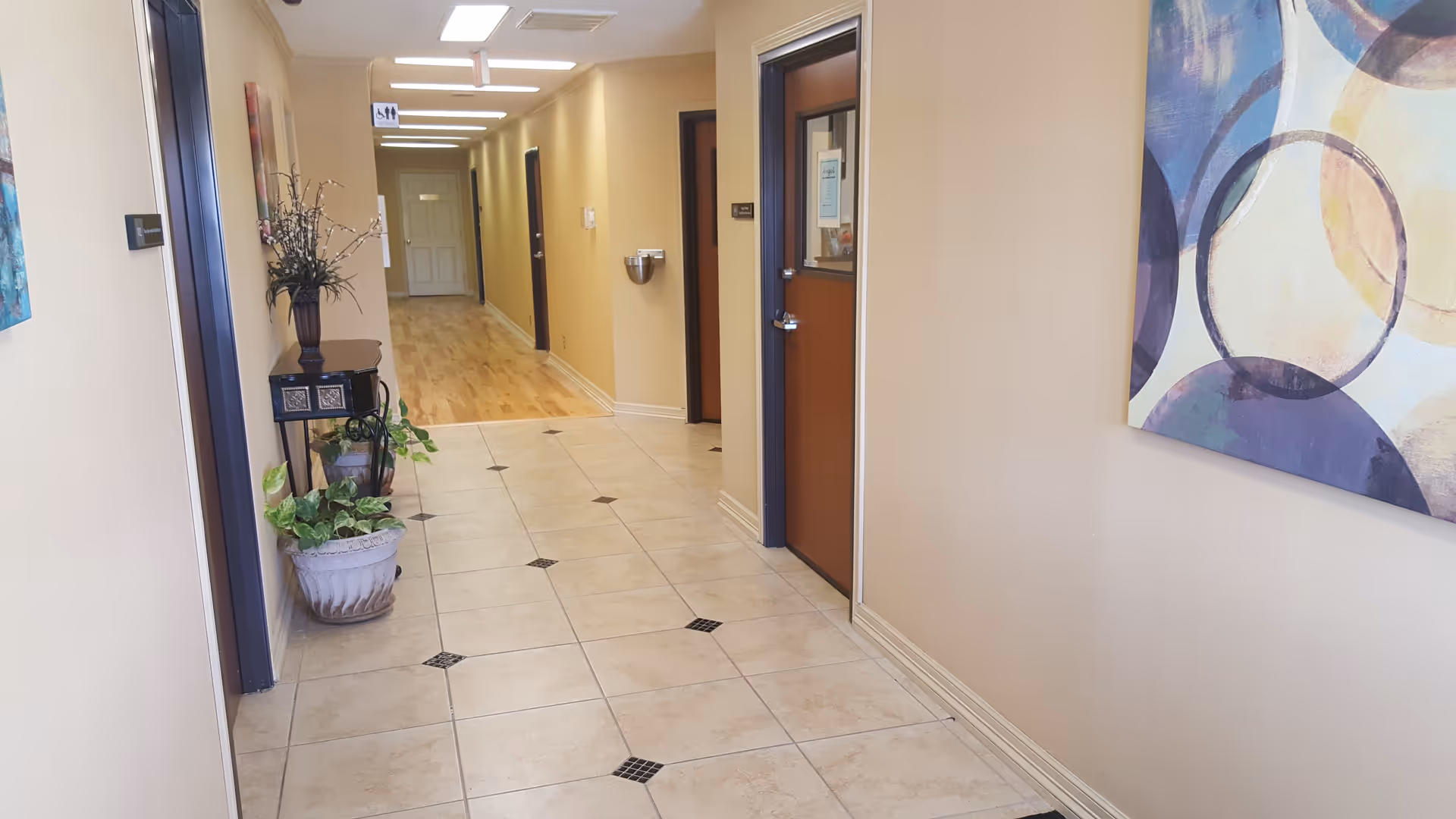 A clean hallway in a senior living facility with beige walls, tiled floor, and artwork.