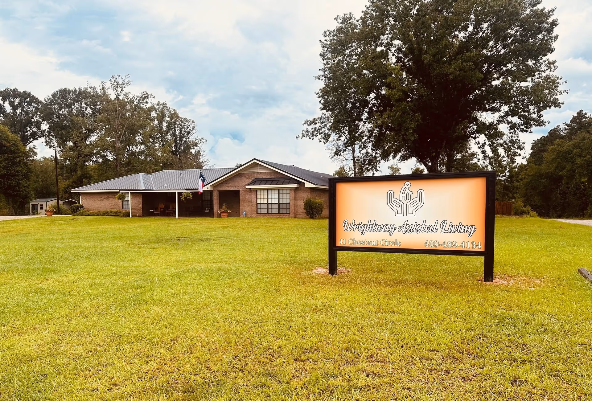 Single-story brick building with an orange sign advertising assisted living amid a green lawn.