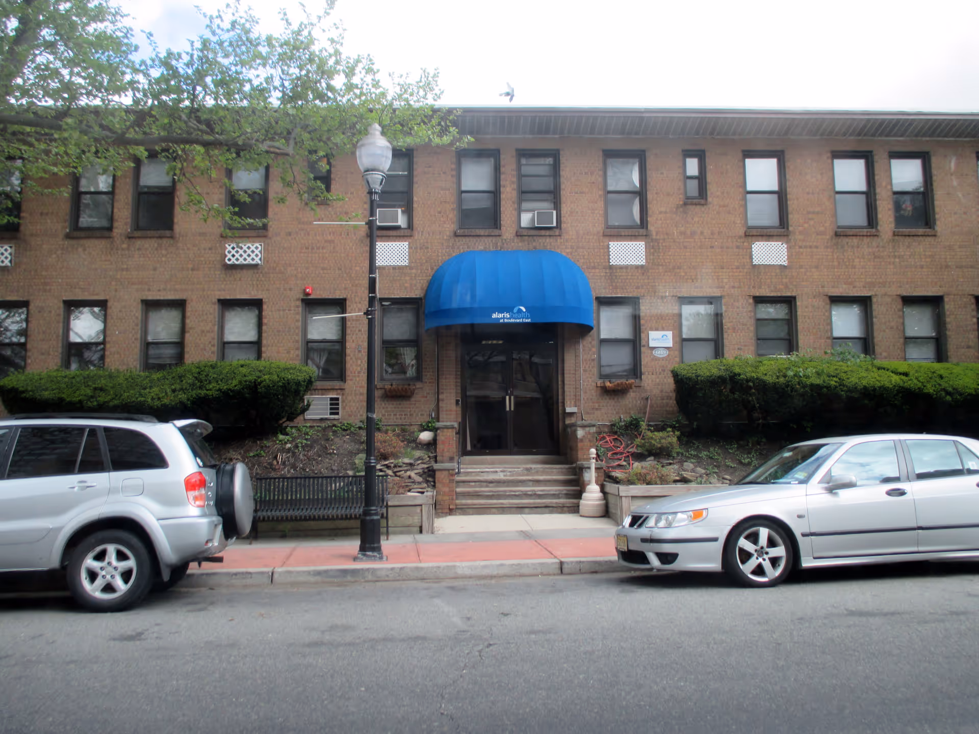 Brick building facade with blue awning over entrance and parked cars along street.