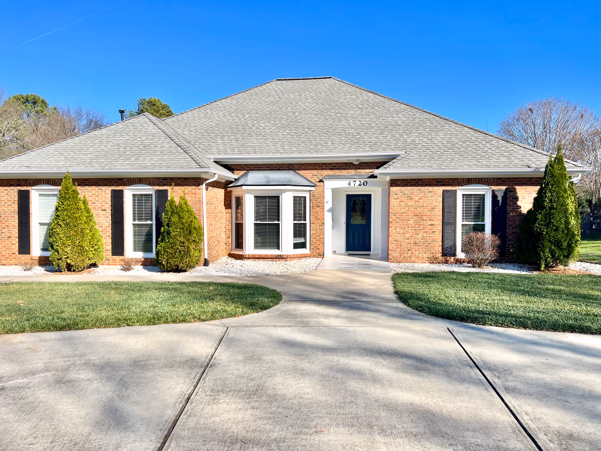 Front view of a brick senior home with blue door, shrubs, and curved walkway.