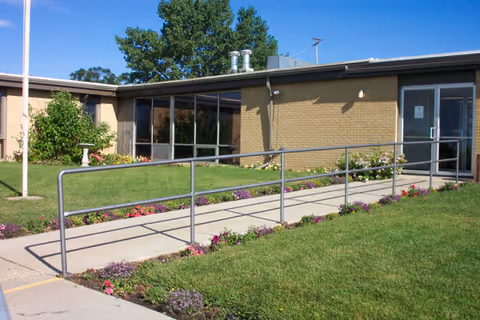 Exterior view of a senior care facility with a ramp and landscaped entrance.