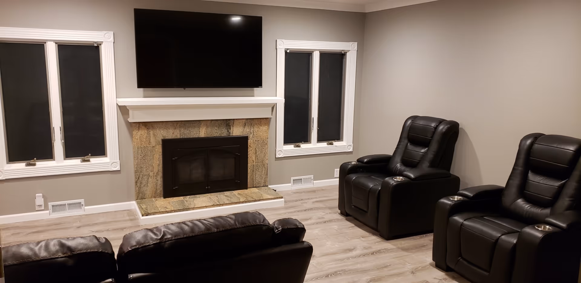 Living room with a stone fireplace and wall-mounted TV, facing black leather recliners and a sofa.