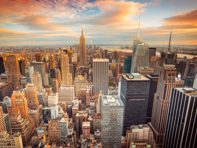 Aerial view of a dense city skyline with skyscrapers bathed in sunset light.