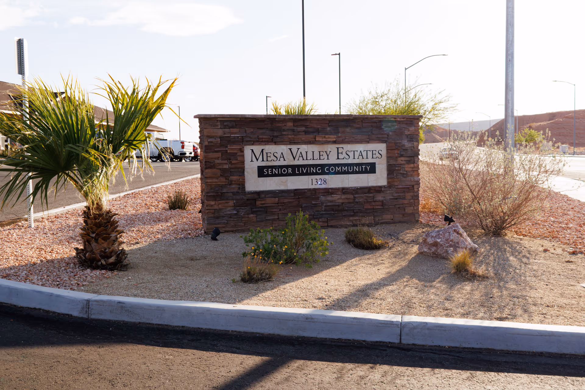 Stone sign for Mesa Valley Estates Senior Living Community amid desert landscaping.
