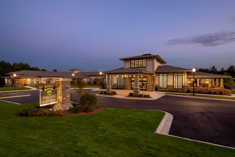 Exterior view of The Birches at Villa Rica with lit entrance and landscaped grounds.