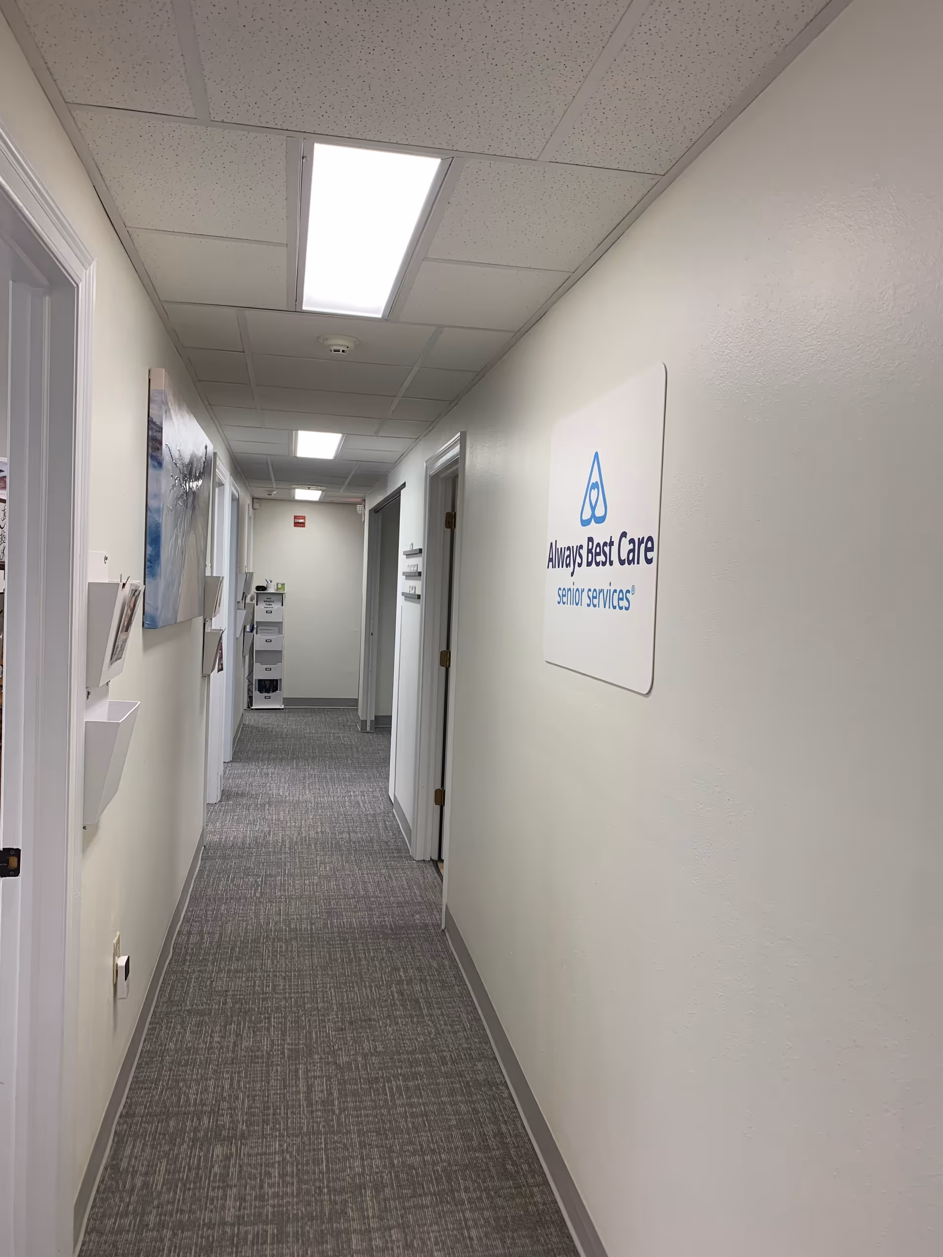 Long well-lit hallway in a senior care facility with doors and a wall sign.