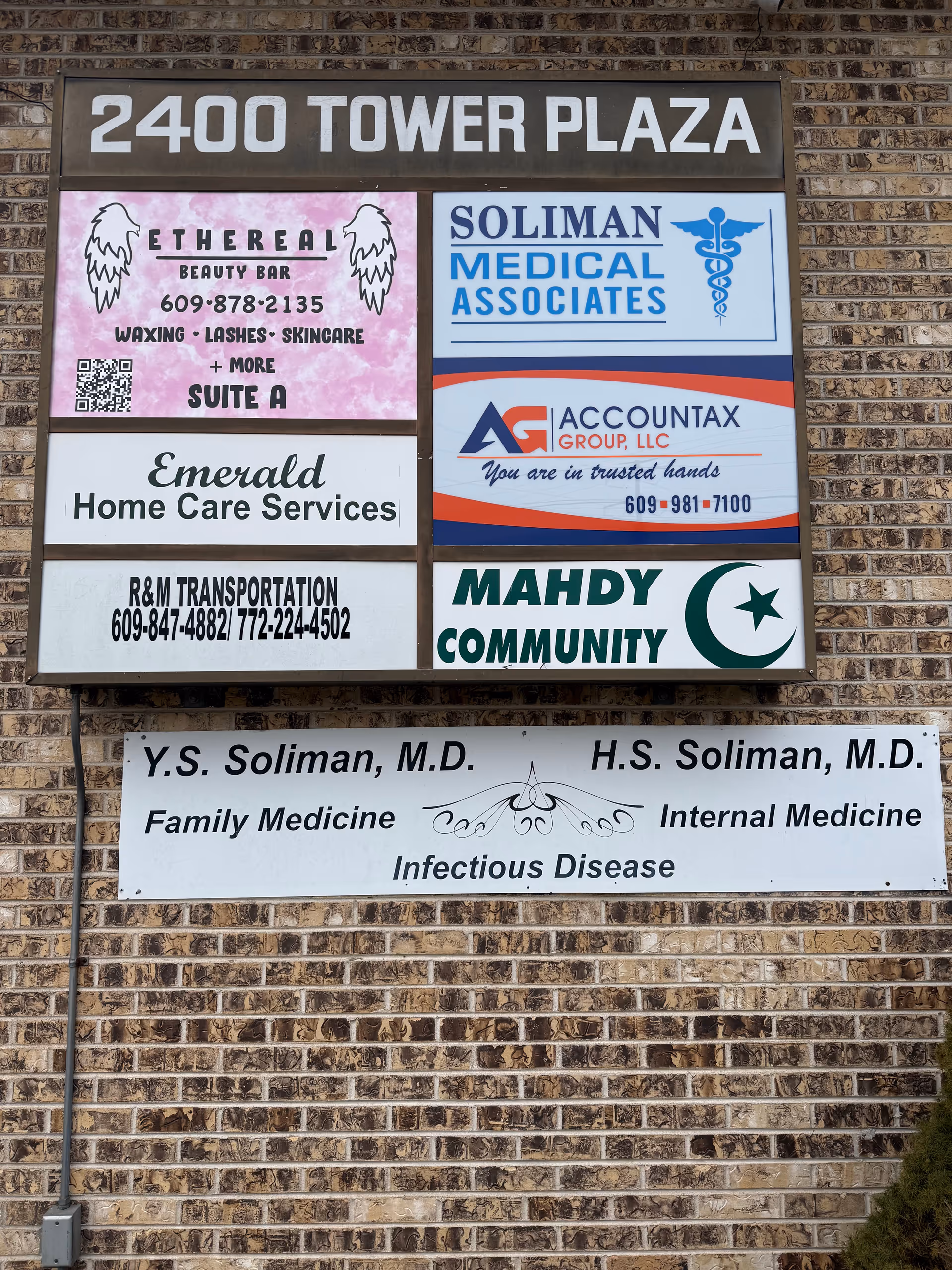 Brick exterior wall with a large multi-sign signboard listing several businesses.