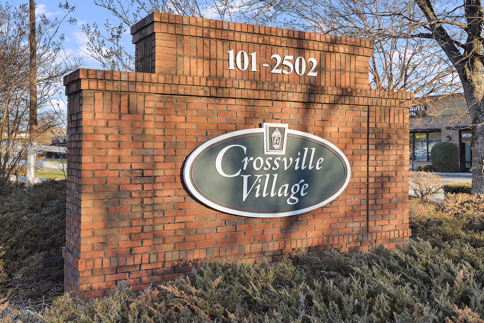 Exterior brick sign reads Crossville Village with numbers 101-2502, surrounded by shrubs.